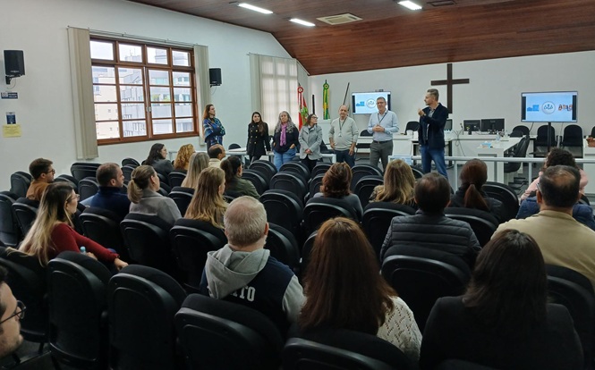 Foto horizontal: autoridades se apresentam à plateia em auditório, público atento acompanha, clima de diálogo e integração institucional.