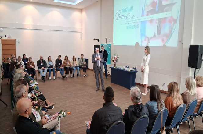 Foto horizontal: facilitadores conduzem atividade do programa Bem-Estar no Trabalho, participantes em círculo acompanham, ambiente amplo, clima de diálogo e integração.