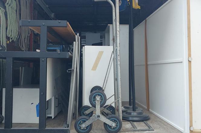 Foto horizontal: móveis, equipamentos e utensílios organizados no compartimento de caminhão durante transporte de bens destinados à doação institucional.