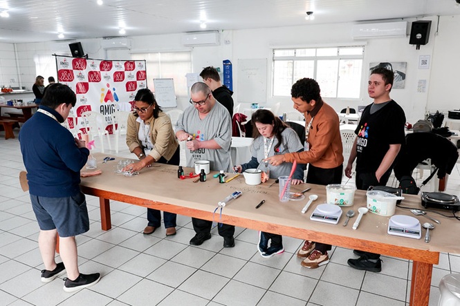 Foto horizontal: jovens participam de atividade prática em oficina, acompanhados por instrutores durante o manuseio de materiais.