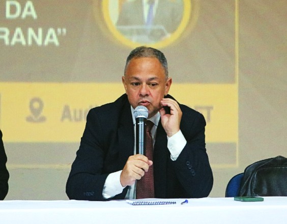Foto horizontal: Juiz Edison Alvanir Anjos de Oliveira Júnior fala ao microfone durante roda de conversa sobre violência doméstica.