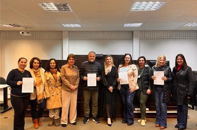 Foto horizontal: participantes exibem certificados durante cerimônia de conclusão de curso promovida na comarca, ao lado de organizadores do evento.