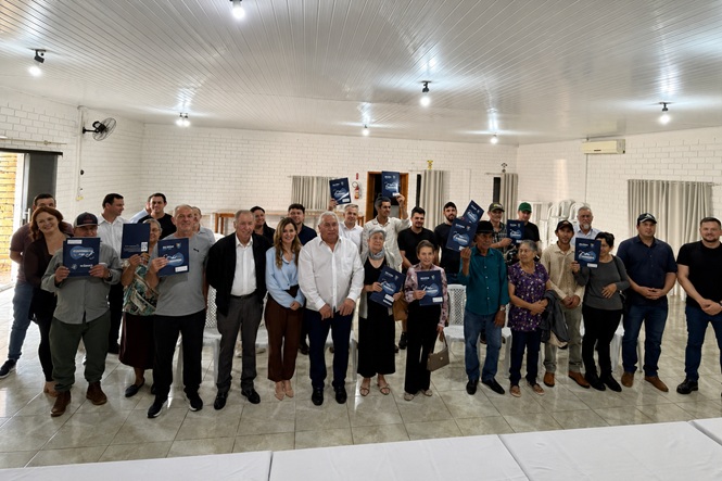 Foto horizontal: grupo de homens e mulheres posa em salão, com alguns participantes segurando cartilhas azuis diante do corpo.