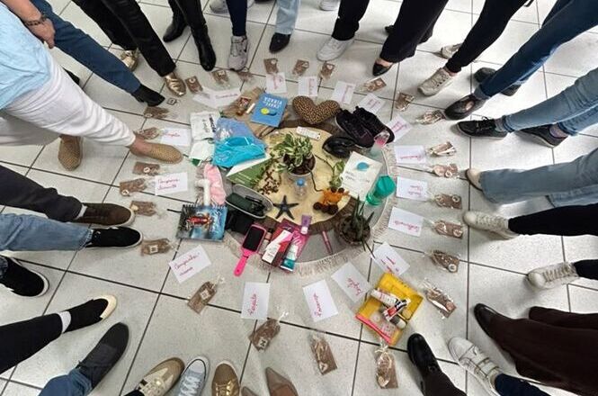 Foto horizontal: participantes formam um círculo em torno de objetos usados em dinâmica