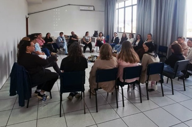 Foto horizontal: participantes estão reunidos em círculo durante atividade voltada ao diálogo e à construção coletiva.