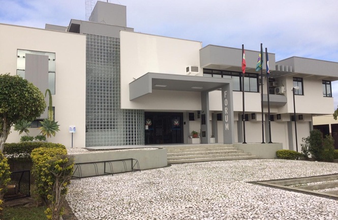 Foto horizontal: fachada do Fórum da comarca de Imaruí, com entrada principal, escadaria e mastros com bandeiras.