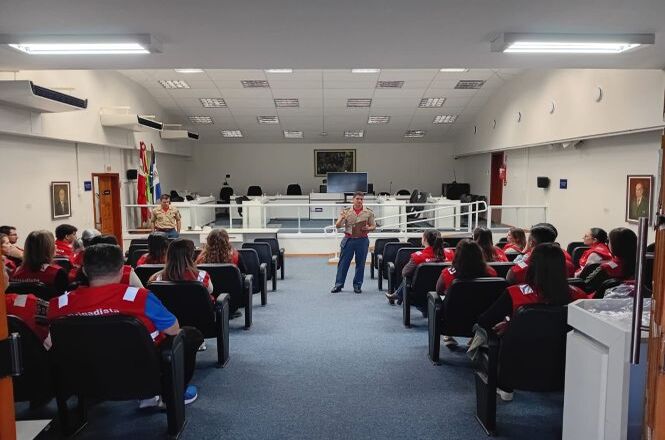 Foto horizontal: participantes acompanham instruções em simulado de evacuação no fórum, equipe organizada em cadeiras, clima de prevenção e segurança.