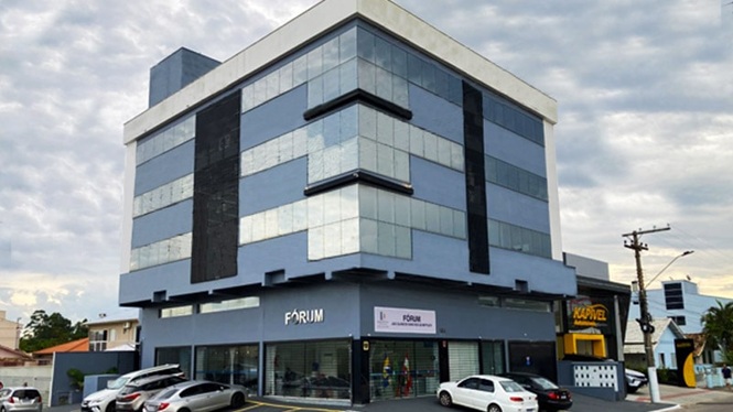 Foto horizontal: fachada do Fórum da comarca de Capivari de Baixo, com entrada principal e veículos estacionados.