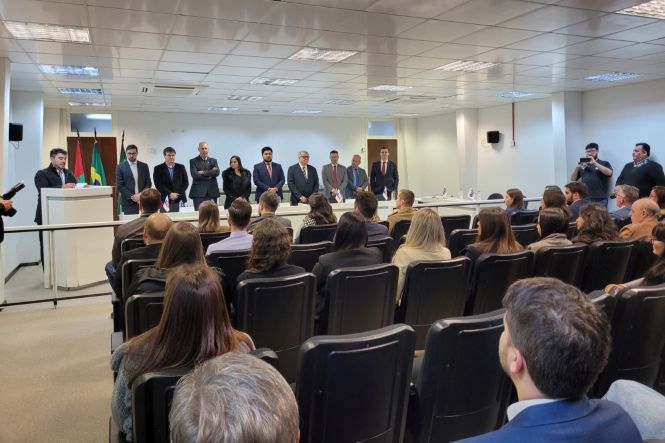 Foto horizontal: autoridades e convidados acompanham solenidade em homenagem ao juiz aposentado Renato Bratti, realizada em auditório do Poder Judiciário.