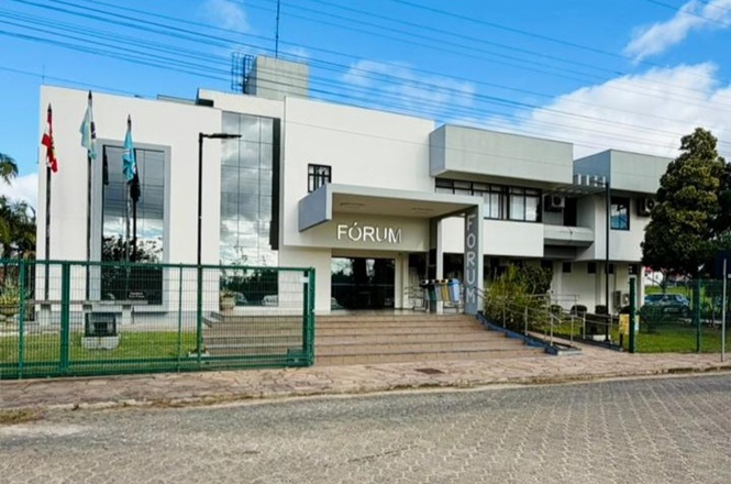 Foto horizontal: fachada do fórum de Içara, prédio institucional moderno com acesso em destaque, clima de acesso à Justiça.