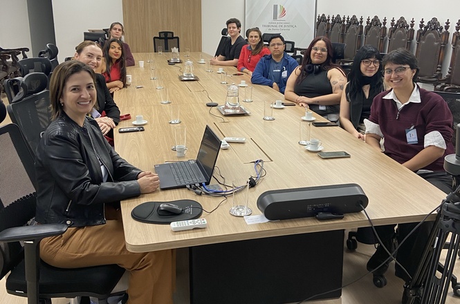 Foto horizontal: grupo de visitantes posa reunido em sala de reuniões do TJSC após visita institucional.