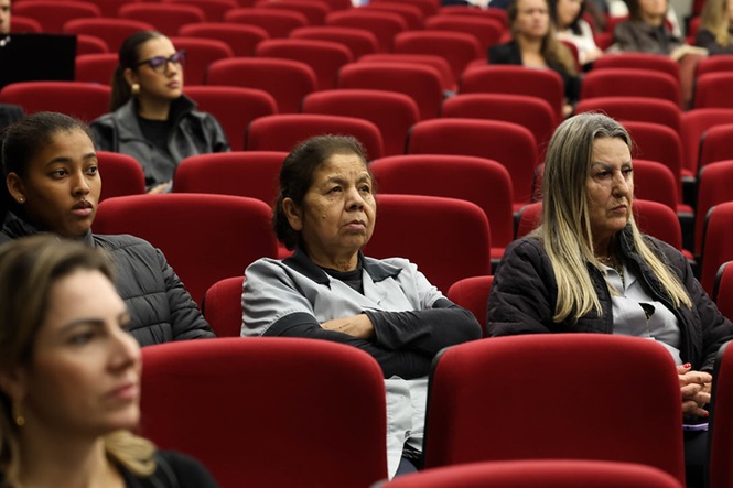 Público acompanha atento palestra em auditório, expressões sérias refletem impacto e reflexão sobre violência e direitos
