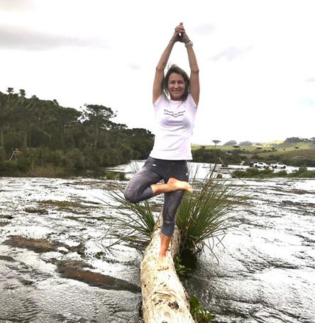 Mulher equilibra-se em tronco sobre rio, em posição de yoga, clima de natureza, concentração e bem-estar