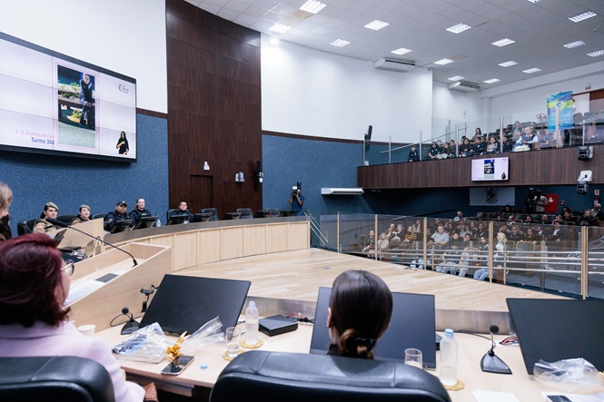 Foto horizontal: público acompanha apresentação no plenário da Câmara de Vereadores de Itajaí, com participantes distribuídos nas galerias e telas de projeção.