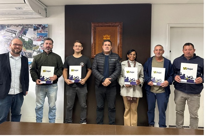 Foto horizontal: sete pessoas posam para registro coletivo, cinco delas segurando cartilhas com identificação de Itajaí.