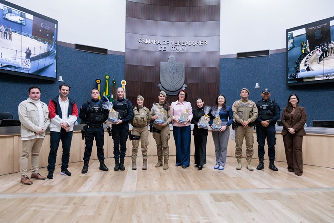 Foto horizontal: grupo de autoridades, policiais e representantes institucionais posa para registro coletivo no plenário da Câmara de Vereadores de Itajaí.