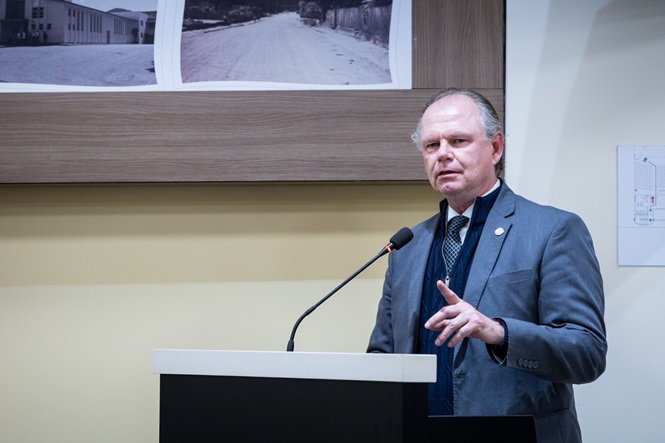 Foto horizontal: presidente do TJSC, desembargador Rubens Schulz, discursa ao microfone no púlpito durante solenidade, com fotografias históricas ao fundo.