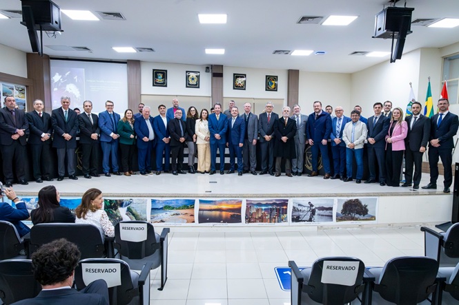 Foto horizontal: desembargador Ricardo Roesler posa com magistrados, autoridades e convidados no plenário, com fotografias de paisagens expostas à frente.