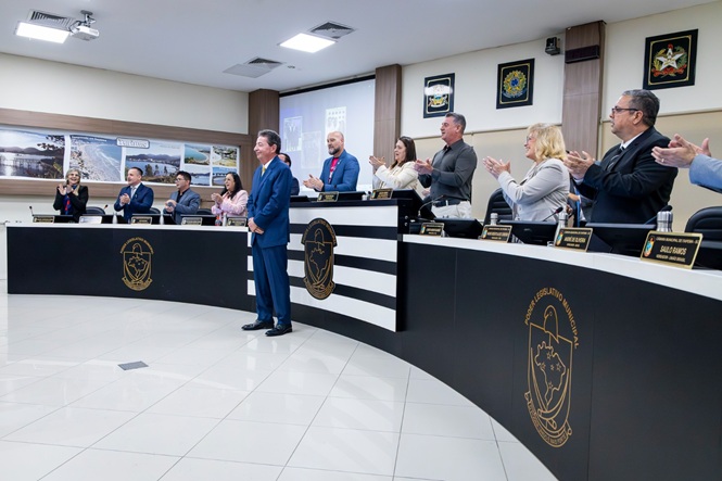 Foto horizontal: desembargador Ricardo Roesler, em pé à frente da mesa, recebe aplausos de magistrados durante sessão no plenário.