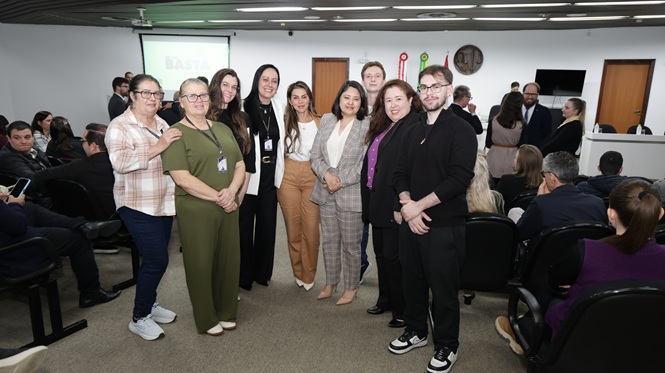 Foto horizontal: grupo de homens e mulheres posa sorridente para registro coletivo em auditório, durante evento institucional.