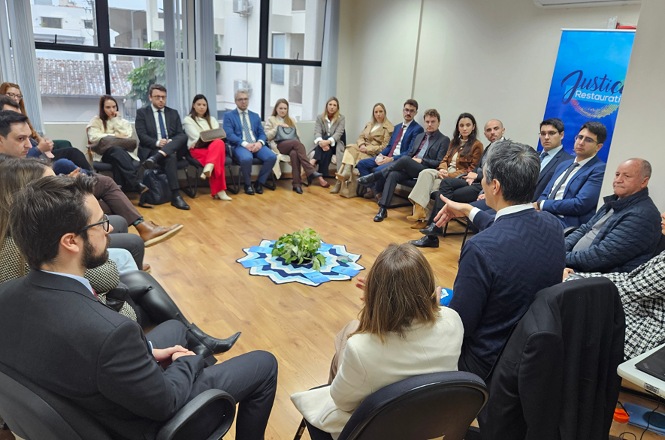 Foto horizontal: reunião institucional com participantes em círculo, debate em andamento, ambiente interno com luz natural, foco no diálogo e escuta.