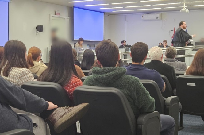 Foto horizontal: público acompanha sessão de julgamento em plenário, enquanto advogado se manifesta diante dos magistrados.