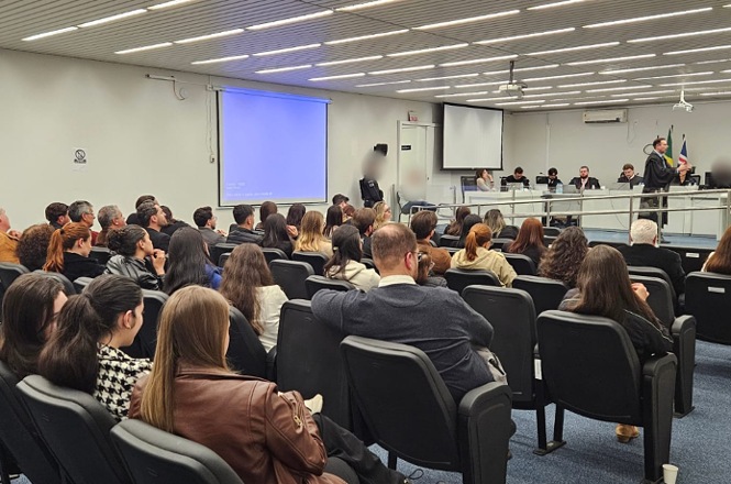 Foto horizontal: público lota o plenário e acompanha sessão de julgamento, enquanto advogado se manifesta diante dos magistrados.