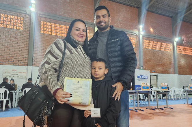 Foto horizontal: família posa com documento em mãos durante atendimento do projeto Justiça até Você, ambiente comunitário, clima de conquista e acolhimento.