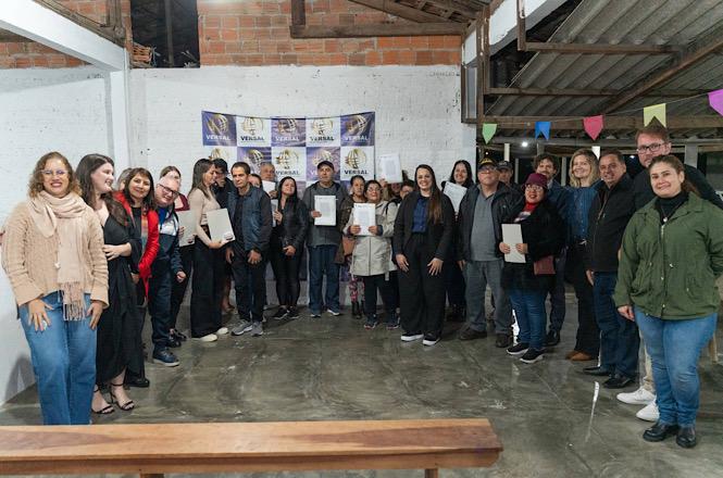 Foto horizontal: participantes do Programa Lar Legal posam com documentos de regularização fundiária durante cerimônia de entrega de títulos em Joinville.