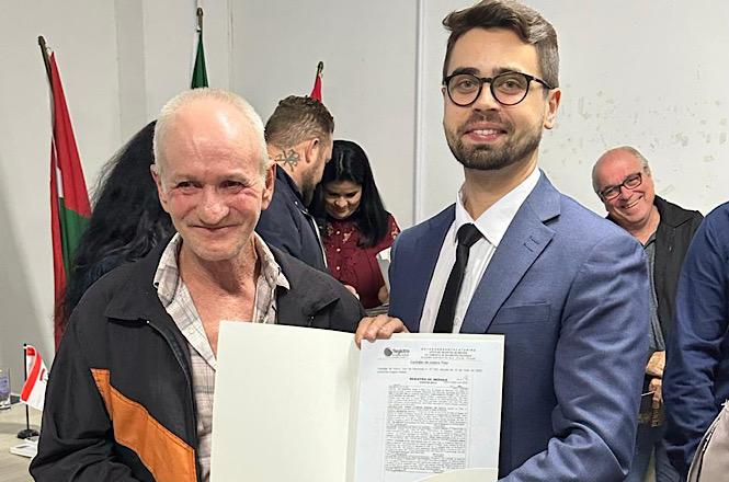 Morador recebe título de propriedade durante entrega de documentos do Programa Lar Legal, em Penha.