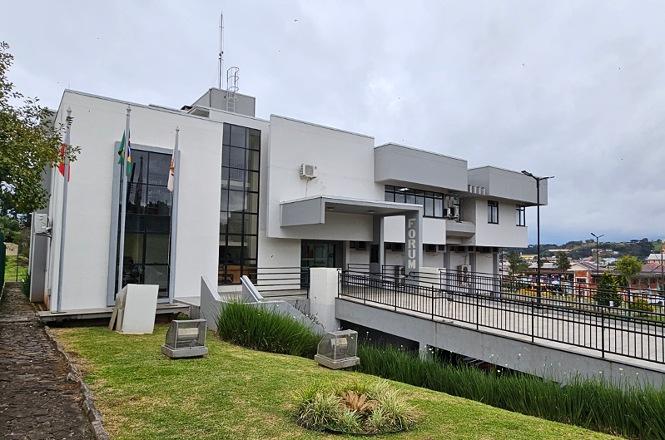Foto horizontal: fachada do Fórum da Comarca de Lebon Régis, com bandeiras, rampa de acesso e jardim na área externa.