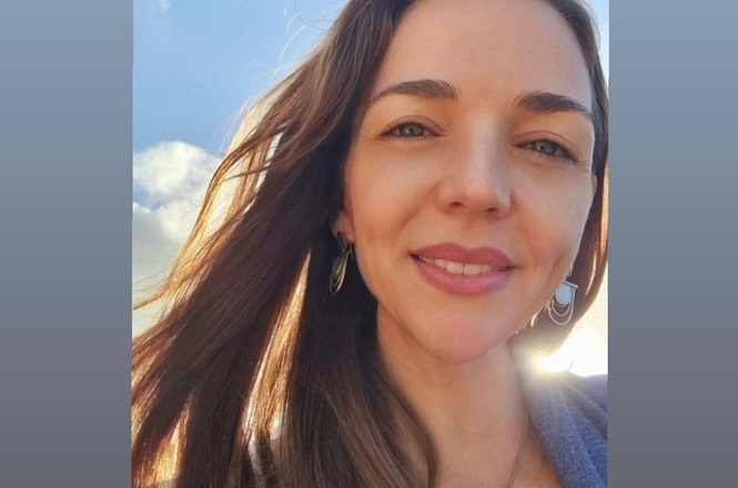 Foto horizontal: psicóloga Luciana Rabello Silva posa sorridente para retrato em área externa, com céu azul ao fundo.