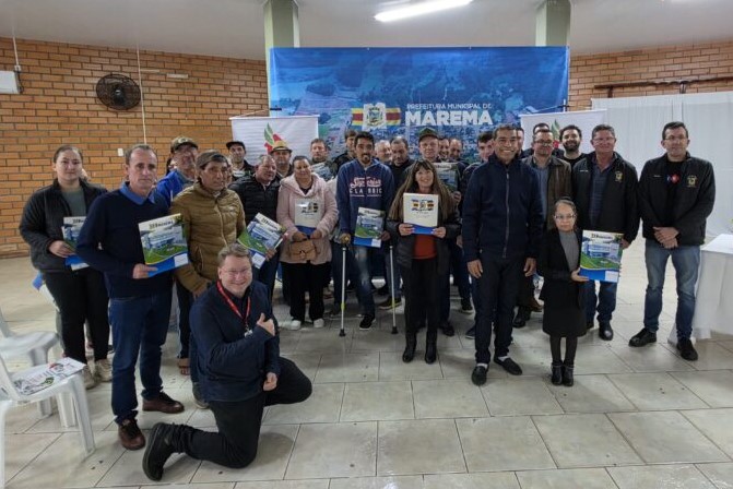 Foto horizontal: grupo posa para registro coletivo, com participantes exibindo cartilhas durante atividade na Prefeitura Municipal de Marema.