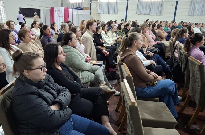 Imagem horizontal mostra público sentado em auditório, acompanhando palestra durante evento institucional.