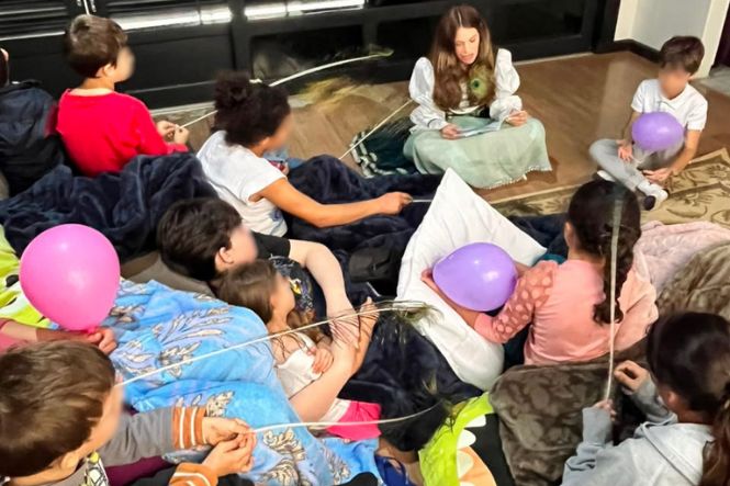 Foto horizontal: crianças participam de roda de leitura com balões e penas durante atividade recreativa.