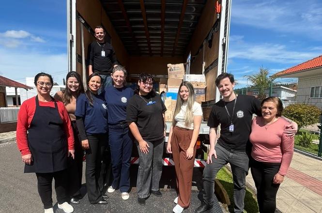 Foto horizontal: equipe posa diante de caminhão com caixas de arquivo durante trabalho de transporte e organização.