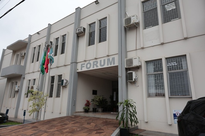 Foto horizontal: fachada do fórum de Palmitos, prédio institucional com bandeiras em destaque, ambiente externo, clima de acesso à Justiça.