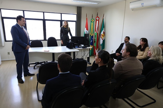 Foto horizontal: homem fala diante de servidores reunidos em sala do Fórum, com bandeiras do Brasil e de Santa Catarina ao fundo.