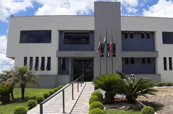 Foto horizontal: fachada do fórum de Papanduva, prédio institucional com acesso central e área verde em destaque, clima de acesso à Justiça.