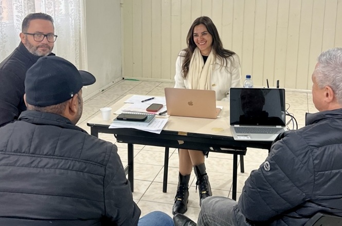 Foto horizontal: equipe realiza atendimento a moradores em ação de regularização fundiária, com orientação e análise documental em ambiente comunitário.