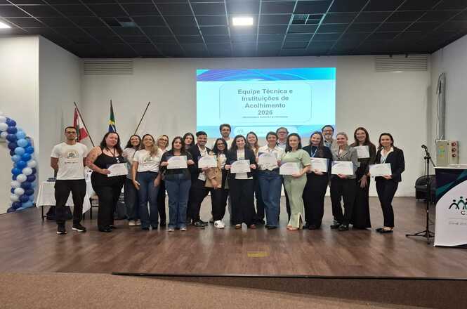 Foto horizontal: integrantes da equipe técnica e de instituições de acolhimento posam com certificados durante evento do programa Novos Caminhos, em Brusque.