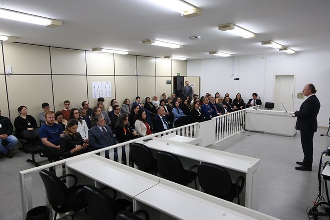 Foto horizontal: presidente do TJSC, desembargador Rubens Schulz, fala diante de autoridades e servidores reunidos em sala de audiência do Fórum.