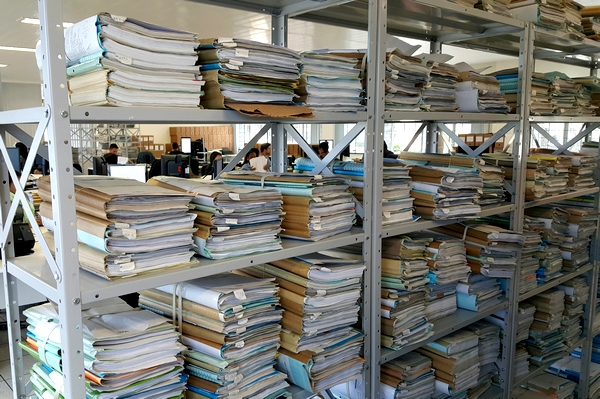 Foto horizontal: estantes metálicas armazenam grande quantidade de processos físicos e documentos empilhados.