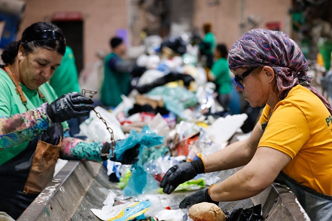 Foto horizontal: trabalhadores realizam triagem de materiais recicláveis em esteira, atividade em destaque, clima de sustentabilidade e trabalho coletivo.