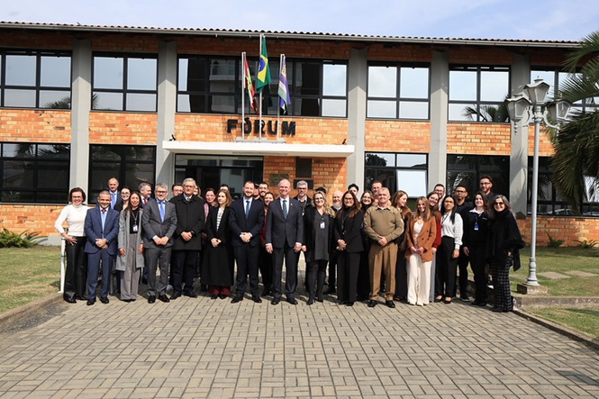 Foto horizontal: grupo de autoridades e servidores posa para registro coletivo em frente ao prédio do Fórum.