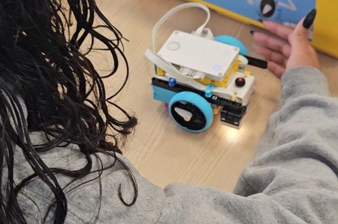 Foto horizontal: estudante interage com robô educacional sobre mesa, equipamento em funcionamento, atividade prática em destaque, clima de aprendizado, experimentação e tecnologia.