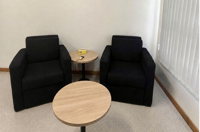 Foto horizontal: sala de depoimento especial com duas poltronas pretas e mesas de apoio.
