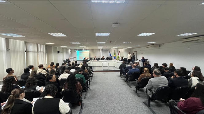Foto horizontal: público acompanha sessão de julgamento em sala com magistrados à frente.