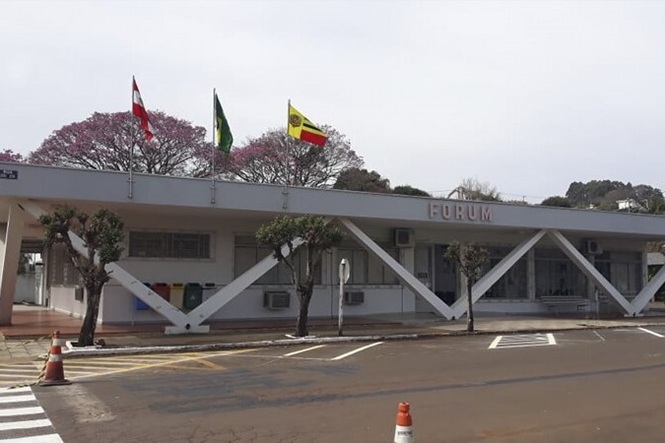 Foto horizontal: fachada do Fórum da comarca de São José do Cedro, com entrada principal e mastros com bandeiras.