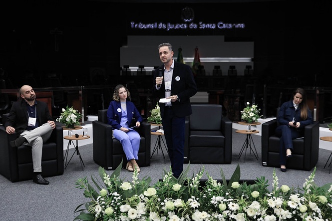 Foto colorida: painel de debatedores em plenário do TJSC, ambiente institucional interno, evento sobre saúde mental, discutindo temas em preto, azul e branco